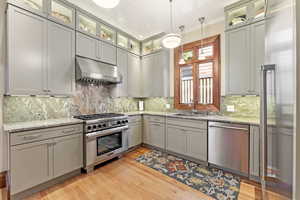 Kitchen with light stone countertops, sink, stainless steel appliances, pendant lighting, and light hardwood / wood-style floors