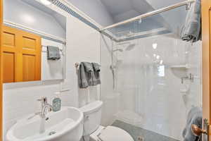 Bathroom with vaulted ceiling, a shower with door, sink, tile walls, and toilet