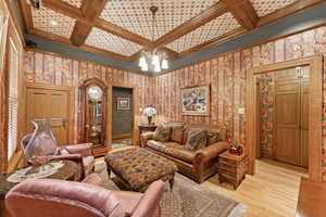 Living room with a notable chandelier, beam ceiling, light wood-type flooring, and coffered ceiling