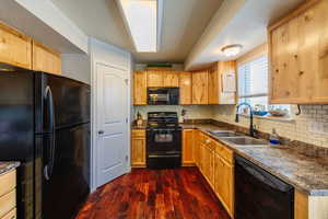 Kitchen featuring black appliances, acacia wood floor., decorative backsplash, and sink