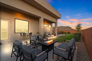 Patio terrace at dusk featuring exterior bar, a yard, and an outdoor living space with a fire pit