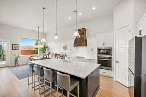 Kitchen featuring white cabinets, decorative light fixtures, a kitchen island with sink, and appliances with stainless steel finishes