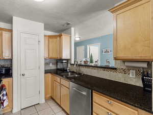 Kitchen with under counter sink, stainless steel dishwasher, dark stone counters, decorative backsplash, and light tile patterned floors