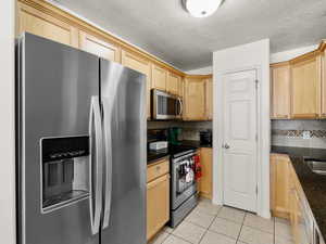 Kitchen with light brown cabinetry, stainless steel appliances, tasteful backsplash, and light tile patterned flooring