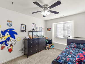 Bedroom with ceiling fan, light colored carpet, and a textured ceiling