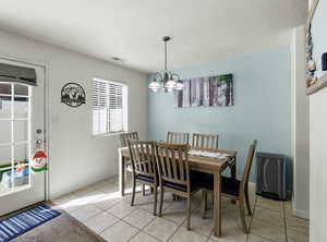 Dining space with light tile patterned floors, a chandelier, and a door leading to the fenced patio