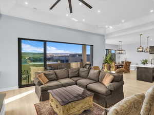 Living room featuring ceiling fan, a raised ceiling, and light wood-type flooring