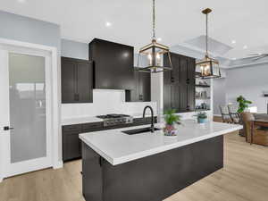 Kitchen with sink, decorative light fixtures, exhaust hood, ceiling fan with notable chandelier, and light wood-type flooring