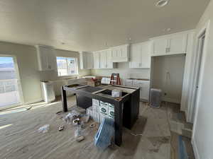 Kitchen featuring a textured ceiling, a kitchen island, white cabinetry, and baseboards