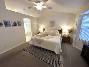 Bedroom featuring ensuite bath, dark carpet, ceiling fan, and lofted ceiling