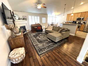 Living room featuring wood-type flooring, a brick fireplace, ceiling fan, and lofted ceiling