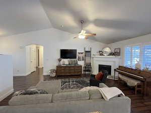 Living room featuring dark wood-type flooring, a brick fireplace, ceiling fan, and lofted ceiling