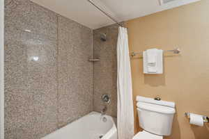 Bathroom featuring shower / bath combination with curtain, toilet, and a textured ceiling