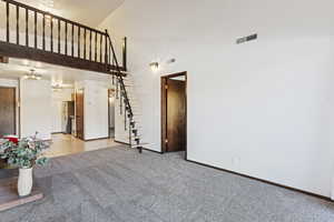 Interior space with a high ceiling, light colored carpet, and an inviting chandelier