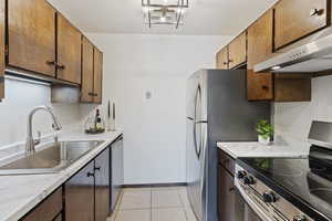 Kitchen featuring ventilation hood, light tile patterned floors, sink, and appliances with stainless steel finishes