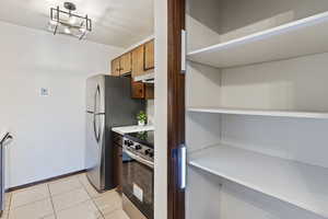 Kitchen with light tile patterned flooring, appliances with stainless steel finishes, pendant lighting, and exhaust hood