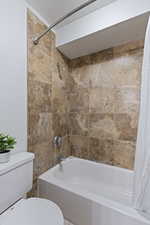 Bathroom featuring toilet and shower / bathtub combination with curtain