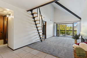 Unfurnished living room with beamed ceiling, light tile patterned floors, and high vaulted ceiling