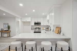 Kitchen with light stone countertops, appliances with stainless steel finishes, white cabinetry, and sink