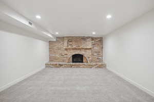 Unfurnished living room with carpet flooring, a fireplace, and brick wall