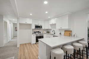 Kitchen with white cabinetry, sink, stainless steel appliances, a kitchen breakfast bar, and light wood-type flooring