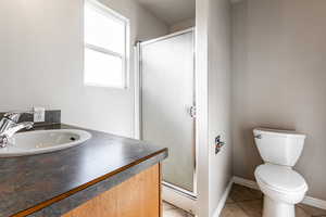 Bathroom featuring baseboard heating, tile patterned floors, a shower with door, and vanity