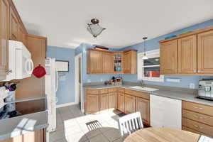 Kitchen with decorative light fixtures, white appliances, sink, and light tile patterned floors