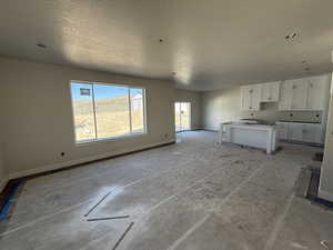 Kitchen featuring open floor plan, a textured ceiling, white cabinets, and baseboards