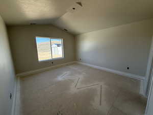 Spare room featuring lofted ceiling, visible vents, baseboards, and a textured ceiling