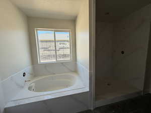 Bathroom featuring a textured ceiling, a marble finish shower, and a garden tub