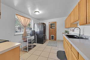 Kitchen with black refrigerator, light tile patterned floors, and sink