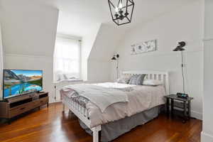 Bedroom with dark hardwood / wood-style flooring, lofted ceiling, and a chandelier