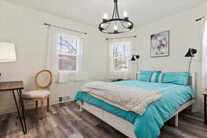 Bedroom with multiple windows, dark wood-type flooring, and an inviting chandelier