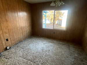 Carpeted empty room featuring wood walls and an inviting chandelier