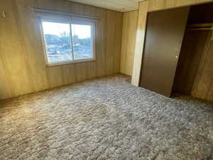 Unfurnished bedroom with carpet, wood walls, and a closet