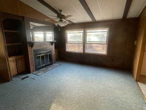 Unfurnished living room with ceiling fan, wood walls, light carpet, and lofted ceiling with beams