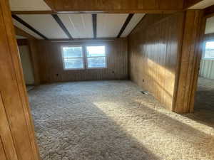 Carpeted empty room with vaulted ceiling with beams and wooden walls