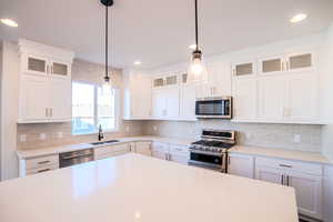 Kitchen featuring decorative light fixtures, stainless steel appliances, and white cabinetry