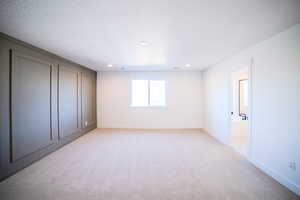 Unfurnished bedroom featuring a textured ceiling, light colored carpet, and ensuite bath