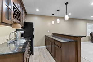 Kitchen featuring sink, light hardwood / wood-style flooring, kitchen peninsula, dark stone countertops, and decorative light fixtures