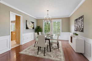 Dining space featuring a textured ceiling, dark hardwood / wood-style flooring, an inviting chandelier, and ornamental molding