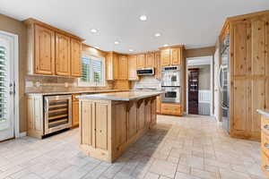 Kitchen featuring appliances with stainless steel finishes, decorative backsplash, a center island, and wine cooler