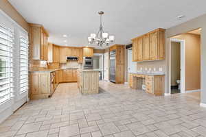 Kitchen featuring light stone counters, stainless steel appliances, light brown cabinets, a chandelier, and a kitchen island