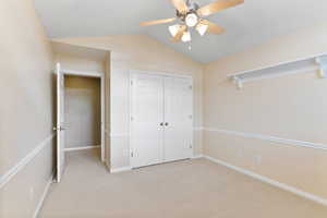 Unfurnished bedroom featuring ceiling fan, a closet, light colored carpet, and lofted ceiling