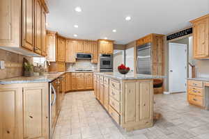 Kitchen featuring light stone countertops, sink, a center island, backsplash, and appliances with stainless steel finishes