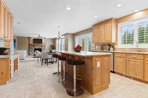 Kitchen with stainless steel dishwasher, light stone counters, pendant lighting, a center island, and a stone fireplace