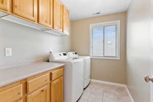 Clothes washing area featuring washing machine and clothes dryer, light tile patterned flooring, and cabinets