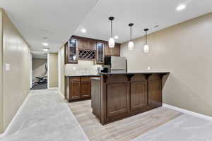 Bar with decorative light fixtures, stainless steel refrigerator, light hardwood / wood-style floors, and sink