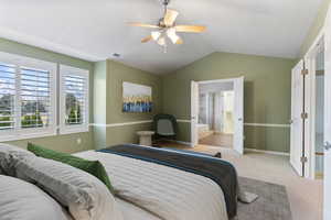 Carpeted bedroom featuring ceiling fan, ensuite bathroom, and lofted ceiling