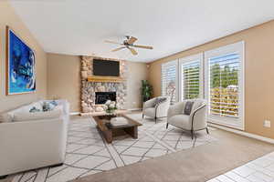 Carpeted living room with a stone fireplace and ceiling fan